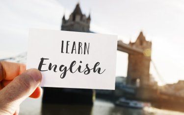 Eine Hand hält eine Karte mit der Aufschrift Englisch lernen vor der verschwommenen Tower Bridge in London.